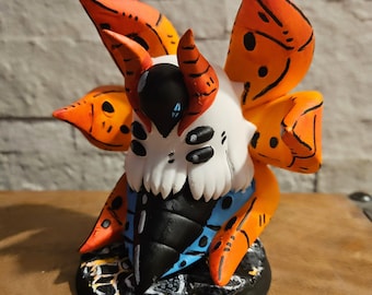 May include: A detailed figurine of a creature with a white head, black eyes, and orange wings. The creature has a black and blue body and is mounted on a black base with yellow and white accents. The wings have black detailing.