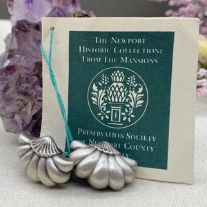 Pode incluir: Dois botões de porta decorativos de prata em forma de flor. Os botões estão sobre uma superfície branca com uma etiqueta que diz "The Newport Historic Collection: From The Mansions Preservation Society of Newport County."