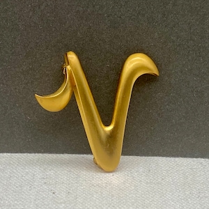Peut inclure: Une broche en métal doré en forme de lettre V avec un design incurvé.