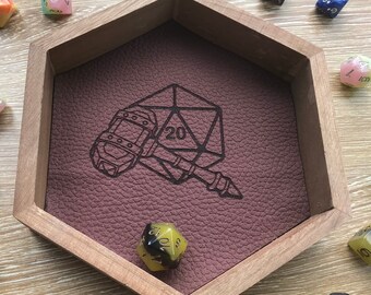 May include: A wooden hexagonal dice tray with a brown leather-like interior. The tray has an engraved design of a hammer and a 20-sided die. There are several colorful dice scattered around the tray.