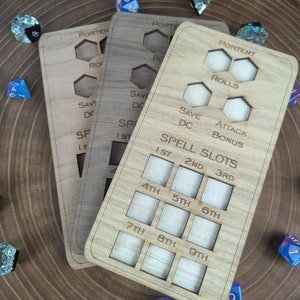 May include: Three wooden spell tracker cards with the text "Portent" and "Rolls" on the top card. The cards have slots for tracking spell slots, save DC, attack bonus, and other game stats.