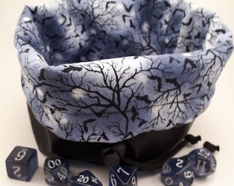 May include: A blue and black fabric dice bag with a drawstring closure. The bag is decorated with a pattern of branches and bats. The bag is filled with blue and silver dice.
