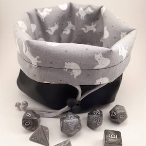 May include: A gray fabric dice bag with a white fox print and a black drawstring. The bag is open and spilling out seven silver metal dice with black numbers.