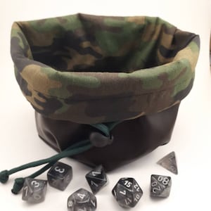 May include: A camouflage fabric dice bag with a brown leather bottom and a green drawstring. The bag is filled with black and white dice.