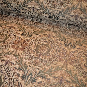 May include: A close-up of a fabric with a brown, green and cream floral pattern. The fabric has a textured surface and a repeating design.