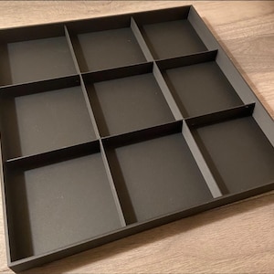 Könnte beinhalten: Ein schwarzes rechteckiges Tablett mit neun quadratischen Fächern. Das Tablett besteht aus einem glatten, harten Material und hat einen leicht erhöhten Rand.