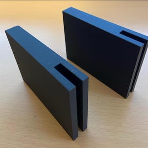 Peut inclure: Deux supports en plastique noir avec une fente découpée au centre. Les supports sont conçus pour maintenir des objets à la verticale.