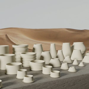 May include: A collection of white ceramic vases and planters of various shapes and sizes, arranged on a gray surface against a backdrop of sand dunes.