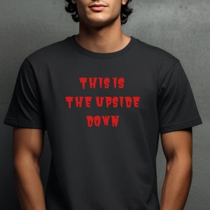 Puede incluir: Una camiseta negra con el texto "THIS IS THE UPSIDE DOWN" en rojo.
