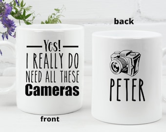 Pode incluir: Caneca de cerâmica branca com um design preto. A frente da caneca diz "Sim! Eu realmente preciso de todas essas câmeras". O verso da caneca tem uma ilustração em preto e branco de uma câmera e o nome "PEDRO" em texto preto.
