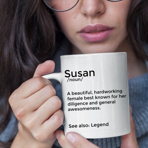 Pode incluir: Caneca de cerâmica branca com um design preto que diz "Susan /substantivo/ Uma mulher bonita, trabalhadora, conhecida por sua diligência e sua geral genialidade. Veja também: Lenda"