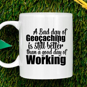 May include: White ceramic coffee mug with a black graphic that reads "A Bad day of Geocaching is still better than a good day of Working".