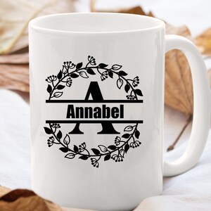 May include: White ceramic mug with a black floral wreath design and the name "Annabel" printed in a split monogram style.