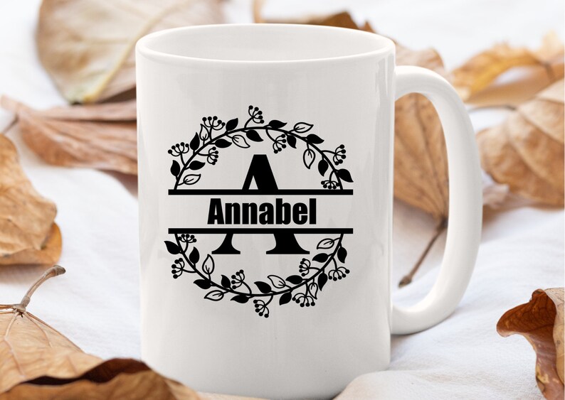 May include: White ceramic mug with a black floral wreath design and the name "Annabel" printed in a split monogram style.
