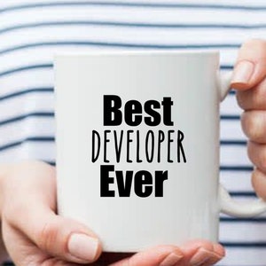 May include: White ceramic mug with black text that reads "Best Developer Ever".