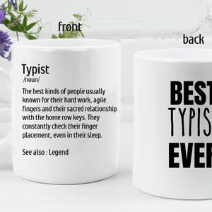 May include: White ceramic coffee mug with a black and white design. The front of the mug has a definition of the word "Typist" and the back of the mug says "Best Typist Ever".