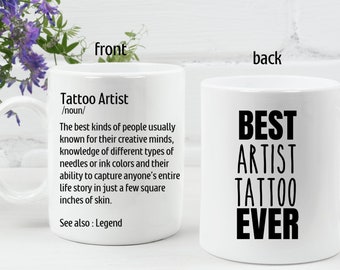 May include: White ceramic mug with the text "Tattoo Artist" and a definition on the front. The back of the mug says "BEST ARTIST TATTOO EVER" in bold black letters. A perfect gift for tattoo artists.