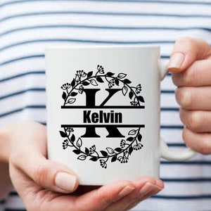 May include: White ceramic mug with a black floral wreath design and the letter "K" in the center. The name "Kelvin" is written below the letter.