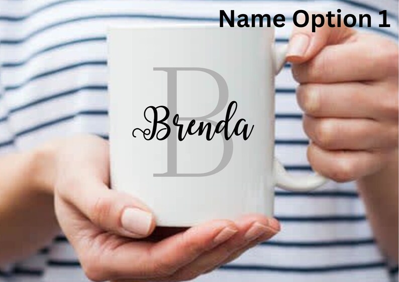 May include: White ceramic mug with the name "Brenda" in a stylish script font, superimposed over a large gray letter "B". The mug is held by a person with a striped background and the text "Name Option 1" at the top.