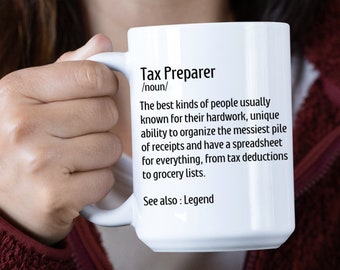 Puede incluir: Taza de cerámica blanca con una definición en blanco y negro de un "Preparador de impuestos" impresa en ella. La definición dice: "Los mejores tipos de personas generalmente conocidos por su arduo trabajo, su capacidad única para organizar la pila más desordenada de recibos y tener una hoja de cálculo para todo, desde deducciones fiscales hasta listas de comestibles. Ver también: Leyenda."