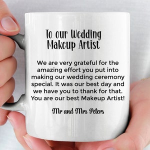 May include: White ceramic mug with a black inscription that reads "To our Wedding Makeup Artist. We are very grateful for the amazing effort you put into making our wedding ceremony special. It was our best day and we have you to thank for that. You are our best Makeup Artist! Mr and Mrs Peters."