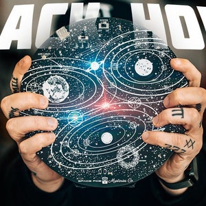 May include: A black circular disc with a white design of a solar system with planets and stars. The disc is being held by a person's hands. The text "BLACK HOLE" is in white letters on a black background above the disc.