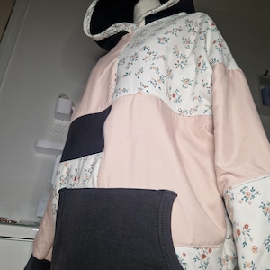 Op de afbeelding: Een patchwork hoodie met een zwarte capuchon en zak. De jas heeft panelen van witte stof met een bloemenpatroon, lichtroze en marineblauw. De mouwen en capuchon zijn gevoerd met een bloemenprint.
