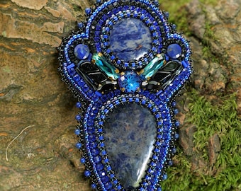 Puede incluir: Un collar con un colgante de cuentas de color azul y negro con dos piedras de lapislázuli. El colgante está colgado de un cordón negro.