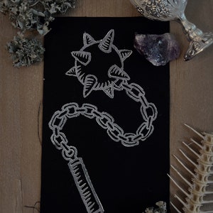 May include: A black patch with a silver embroidered design of a spiked ball attached to a chain and a handle.