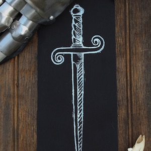 May include: A white chalk drawing of a sword on a black background, with a metal gauntlet and bone fragment. The sword has a detailed hilt and blade. The background is a wooden surface.