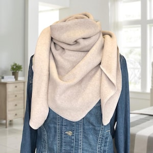 Könnte beinhalten: Ein beiger Fleece-Schal in Dreiecksform. Der Schal ist gefaltet und um den Hals einer Person gelegt.