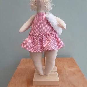 May include: A handmade doll wearing a pink and white polka dot swimsuit and a white towel. The doll has blonde curly hair and is standing on a wooden base.