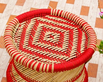 Peut inclure: Un tabouret en bambou tressé avec un motif rouge et crème. Le tabouret a un siège rond.