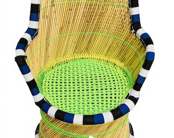 Peut inclure: Une chaise en bambou tressé avec un coussin d'assise tressé vert et blanc. La chaise est ornée d'une bordure en tissu rayé bleu et blanc autour du haut et du bas. La chaise est étiquetée "GUNEE®".