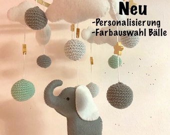 Könnte beinhalten: Ein grauer Filzelefant-Mobile mit weißen Filzohren und einer weißen Filzwolke. Das Mobile enthält außerdem graue, grüne und weiße gehäkelte Kugeln und Holzsterne. Der Text "Neu - Personalisierung - Farbauswahl Bälle" ist im Bild sichtbar.
