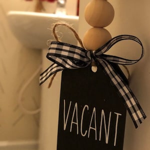 May include: A black sign with the word "VACANT" written in white. The sign is tied to a string of wooden beads with a black and white checkered ribbon.