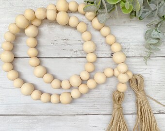 May include: A wooden bead garland with two natural jute tassels. The garland is made of natural wood beads and is perfect for adding a touch of rustic charm to your home decor.