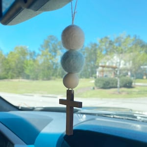 May include: A white, blue, and beige felt ball car charm with a wooden cross hanging from it.
