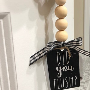 May include: A wooden bead garland with a black and white checkered ribbon and a black tag that says "Did you flush?"