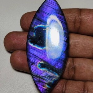 May include: A large, iridescent, purple labradorite gemstone cabochon with a teardrop shape. The stone has a blue and green flash.