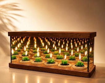 May include: A rectangular wooden frame containing a series of small green succulent-shaped candles with lit wicks. The interior features mirrored panels that create an infinite reflection effect of the candles and their flames within the box.