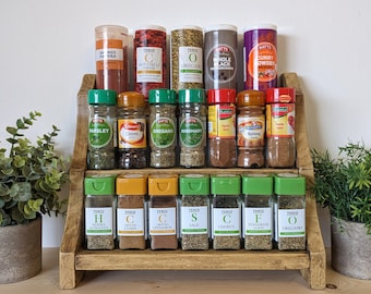 Puede incluir: Un especiero de madera de tres niveles que contiene veintiún frascos de especias variados. Los frascos tienen tapas de varios colores y etiquetas con texto que incluye Smoked Paprika, Hot Chilli Powder, Oregano, Whole Black Peppercorns, Curry Powder, Parsley, Cloves, Rosemary, Paprika, Nutmeg, Herbes de Provence, Cumin, Cinnamon, Sage, Chervil y Fenugreek.