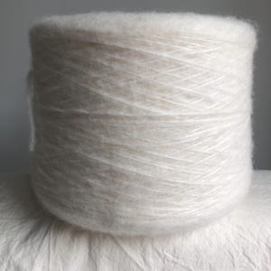 May include: A skein of white yarn, made of a soft, fluffy fiber. The yarn is wound into a ball shape and is ready for knitting or crocheting.