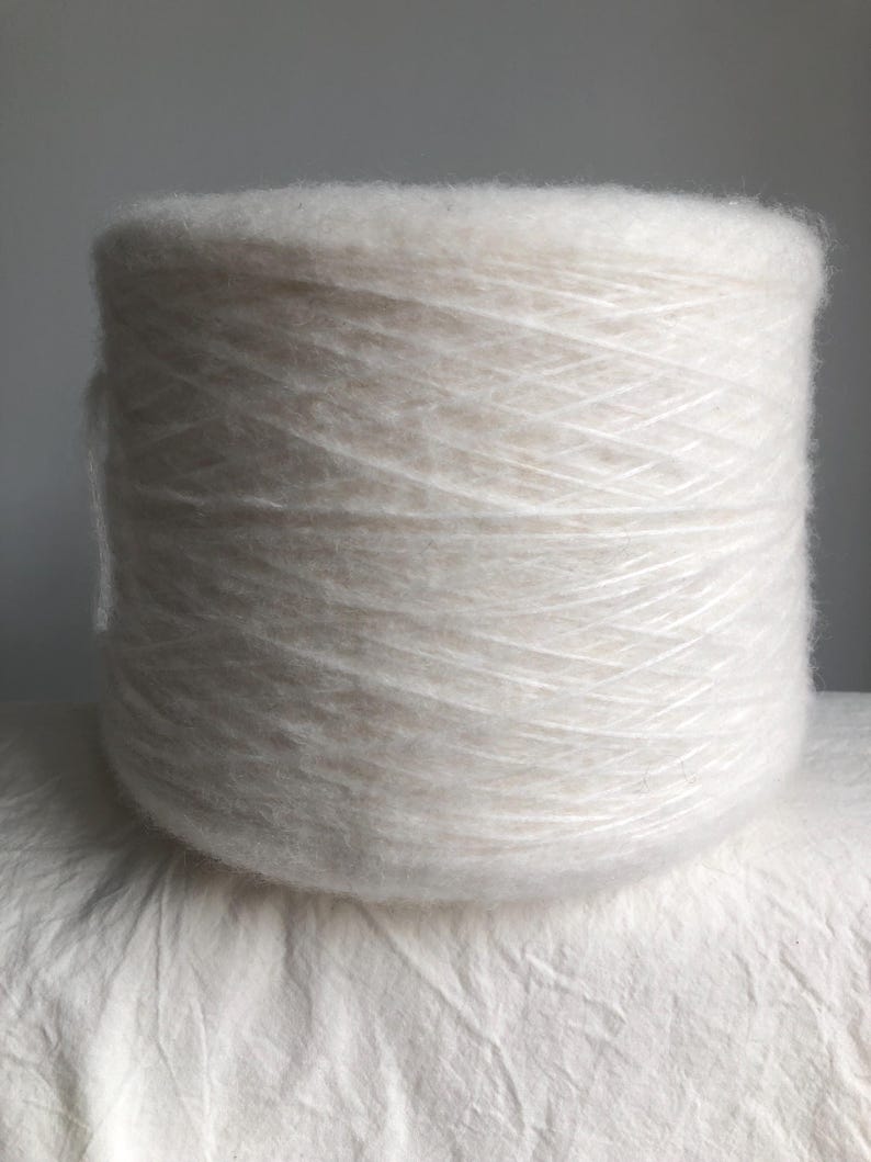 May include: A skein of white yarn, made of a soft, fluffy fiber. The yarn is wound into a ball shape and is ready for knitting or crocheting.