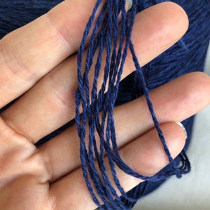 May include: A close-up of a deep blue yarn skein. The yarn is made of natural fibers and has a soft, textured feel.
