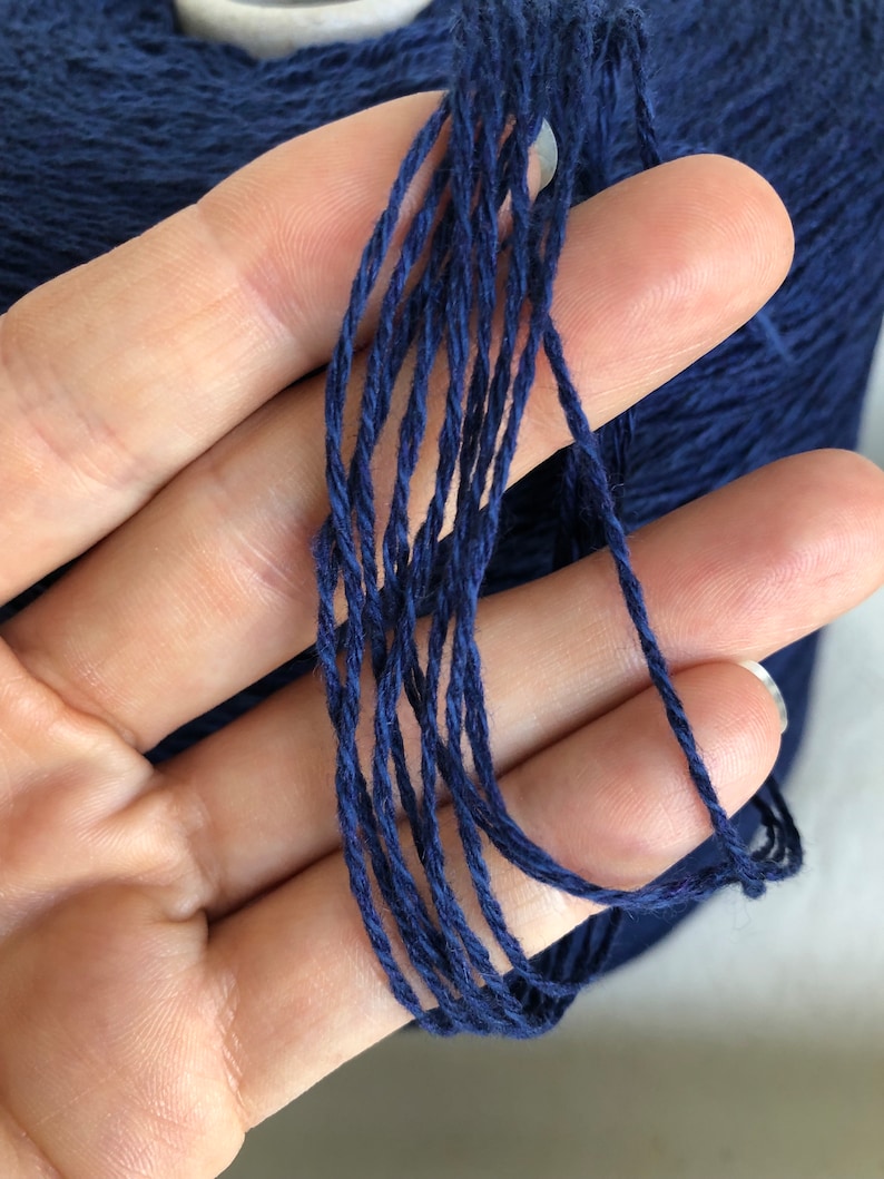 May include: A close-up of a deep blue yarn skein. The yarn is made of natural fibers and has a soft, textured feel.