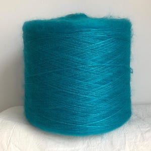 May include: A large spool of teal-colored yarn. The yarn appears soft and fluffy, with visible strands wound tightly together. The color is a vibrant, saturated teal, suitable for knitting or crocheting projects.