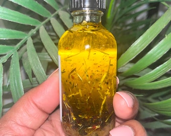 May include: A small glass bottle with a black lid filled with a yellow liquid and herbs. The bottle is being held in a hand.