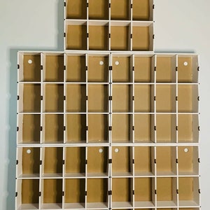 May include: A set of white, modular storage cubes with brown cardboard backing. The cubes are arranged in a stacked configuration, creating a multi-compartment storage unit. Each cube has a small circular opening.