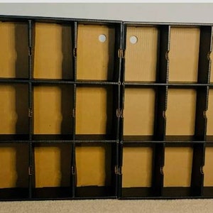 May include: Two black, multi-compartment storage units with cardboard dividers. Each unit has three rows of four compartments. The cardboard dividers are a light brown color, and each compartment has a circular hole at the top.